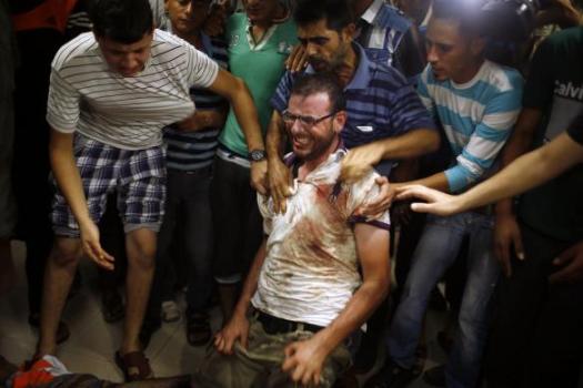 Palestinian man reacts next to the body of his relative, whom medics said was killed by Israeli shelling near a market in Shejaia, at a hospital in Gaza City